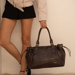 Sac à main Alba chocolat porté à la main, jambes croisées