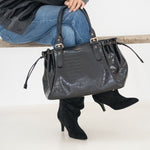 Sac à main Alba noir posé sur un banc, femme assise