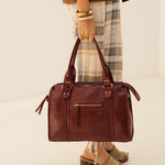 Sac à main Eléa bordeaux porté à la main, femme debout