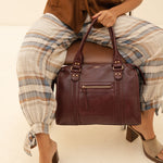 Sac à main Eléa bordeaux tenu à la main, femme assise