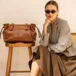 Sac à main Iria camel posé sur un tabouret, femme assise