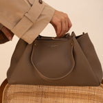 Sac à main Jane taupe posé sur une chaise, main sur l'anse