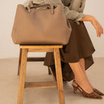 Sac cabas Mary taupe posé sur un tabouret, femme assise