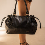 Sac à main Iria noir porté à la main, femme debout